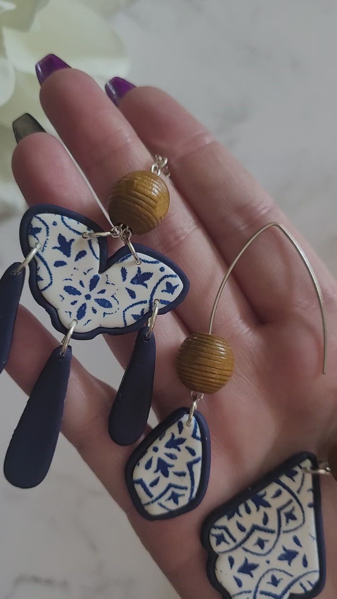 Closeup of different style polymer clay earrings on a white background. Earrings are white and navy with a tile print and wood bead.
