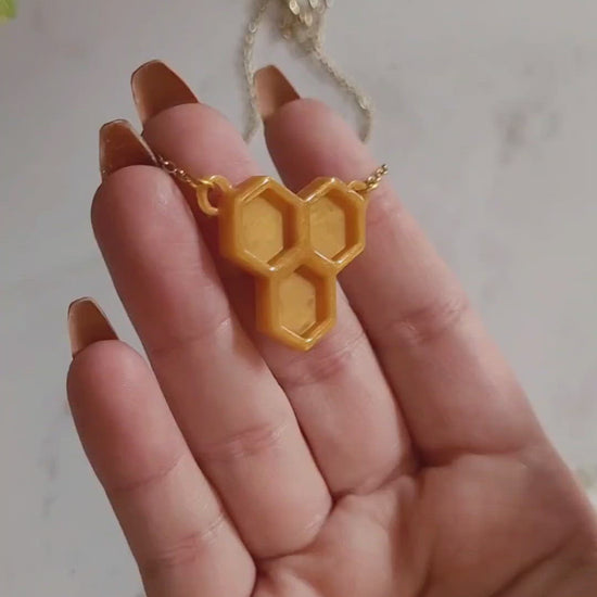 Closeup of honeycomb shaped resin necklace in a hand to show size and color details.