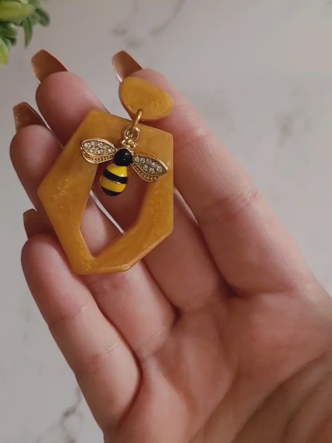 Close up of hexagon shaped resin earring with bee charm in a hand to show size and color detail. 