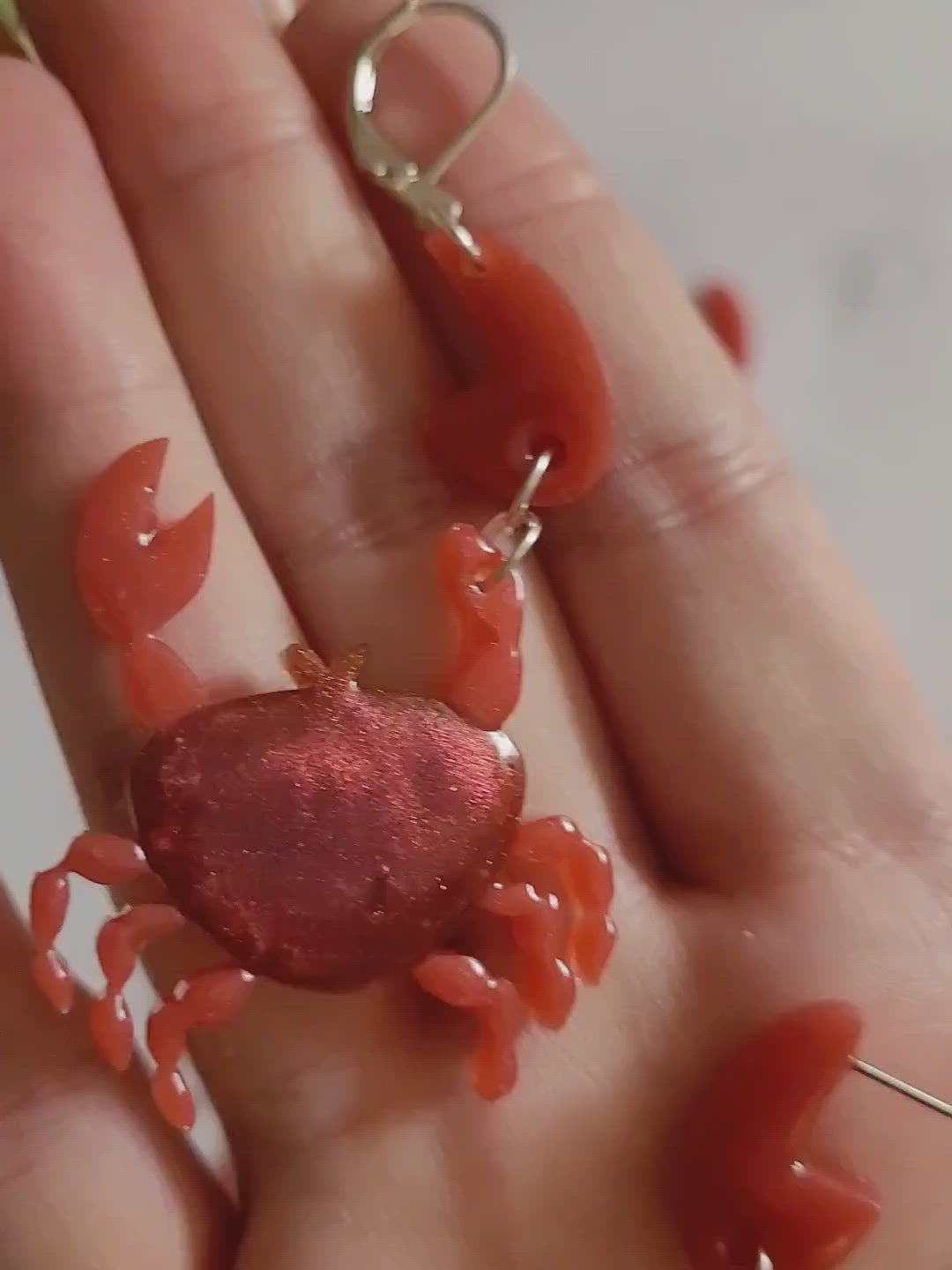 Close up of resin earrings in the shape of a red crab with metallic accents.