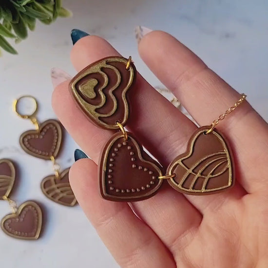 video close up of Chocolate and gold heart truffle necklace on a white background.