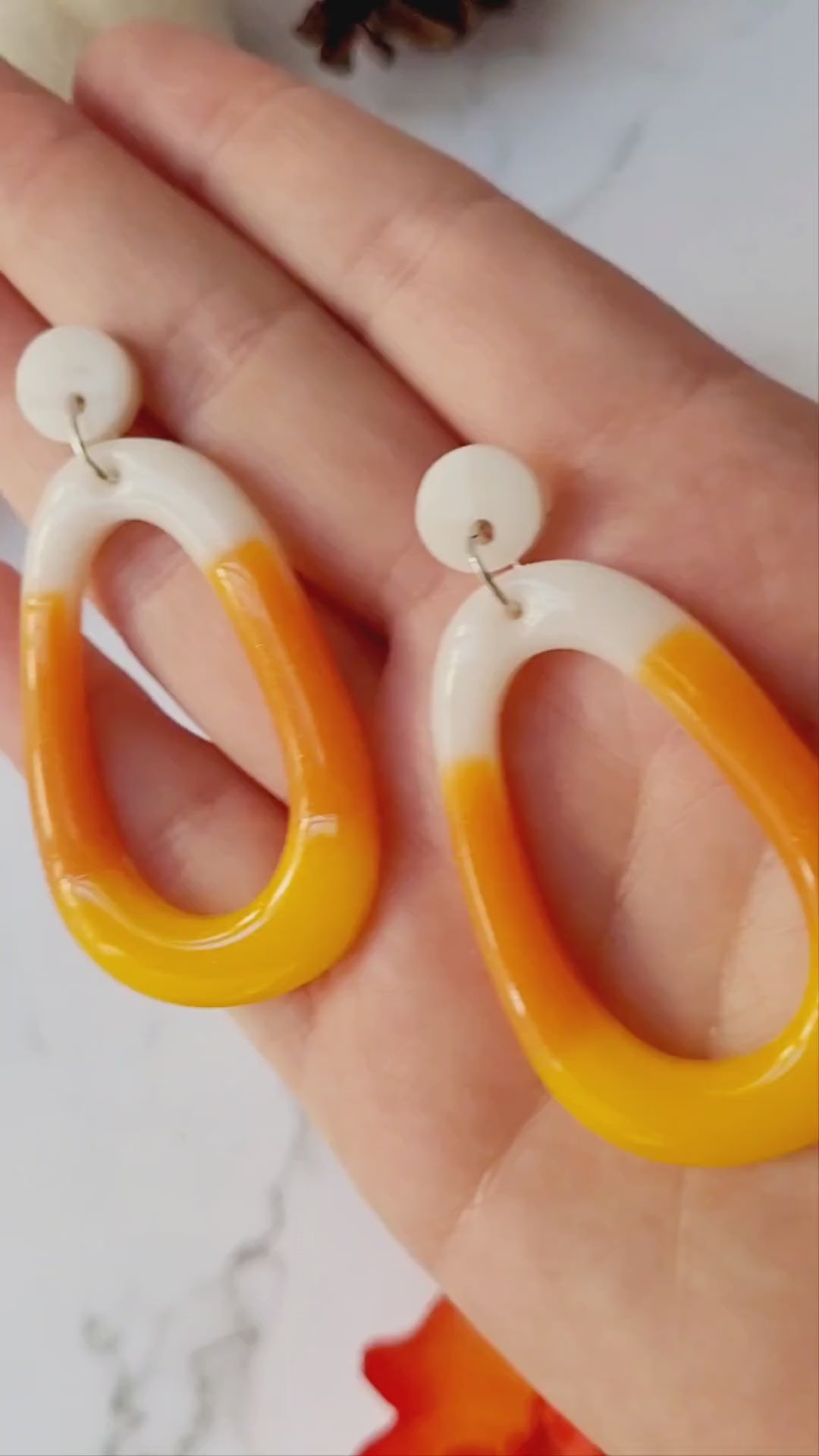 video close up of candy corn colored dangle earrings on a white marble background