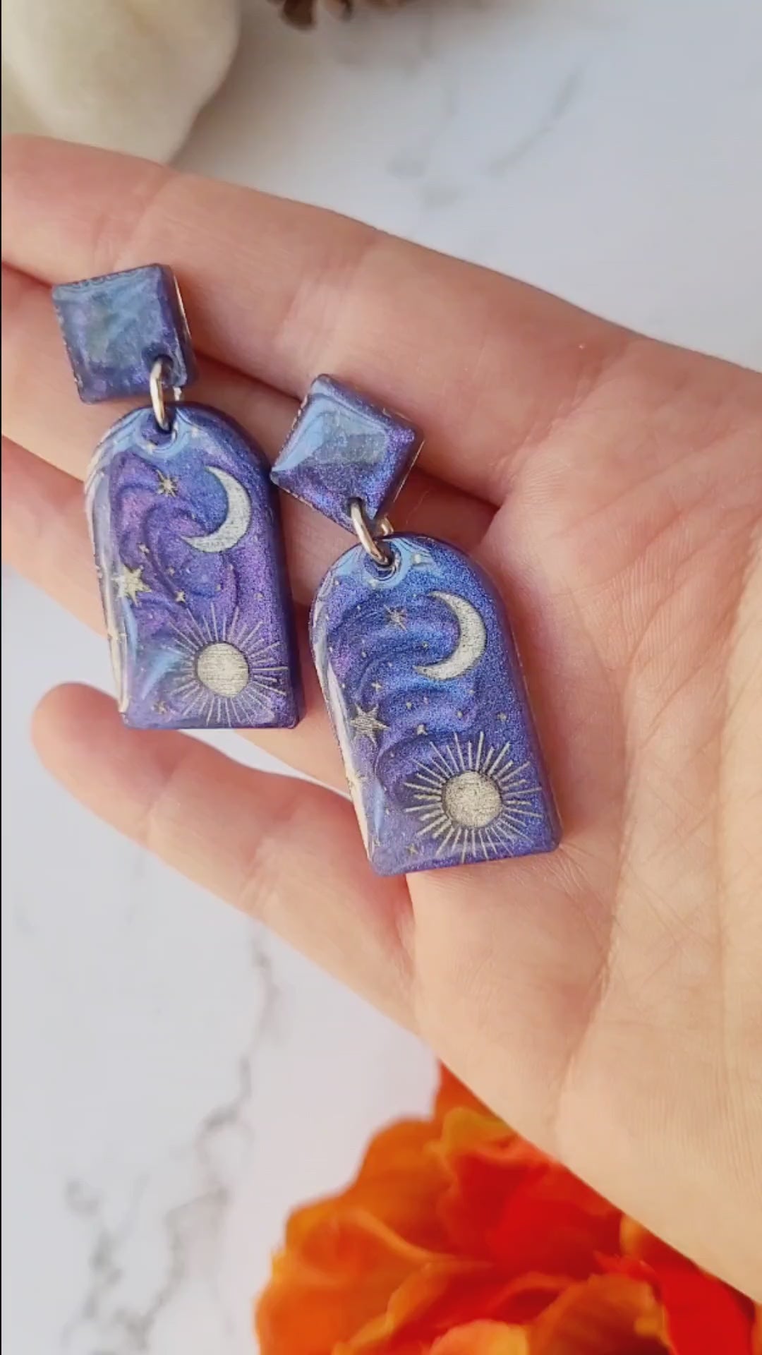 video close up of blue arch earrings with painted celestial details on a marble background.