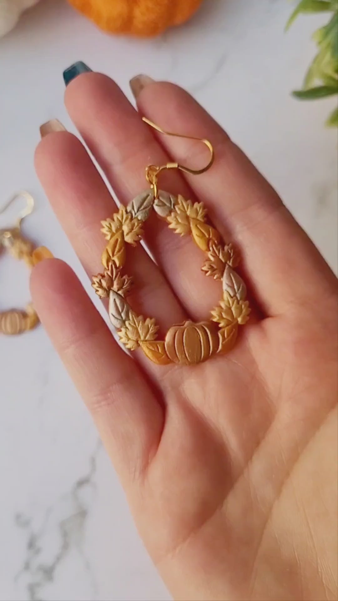 video close up of fall harvest themed teardrop earrings on a marble background