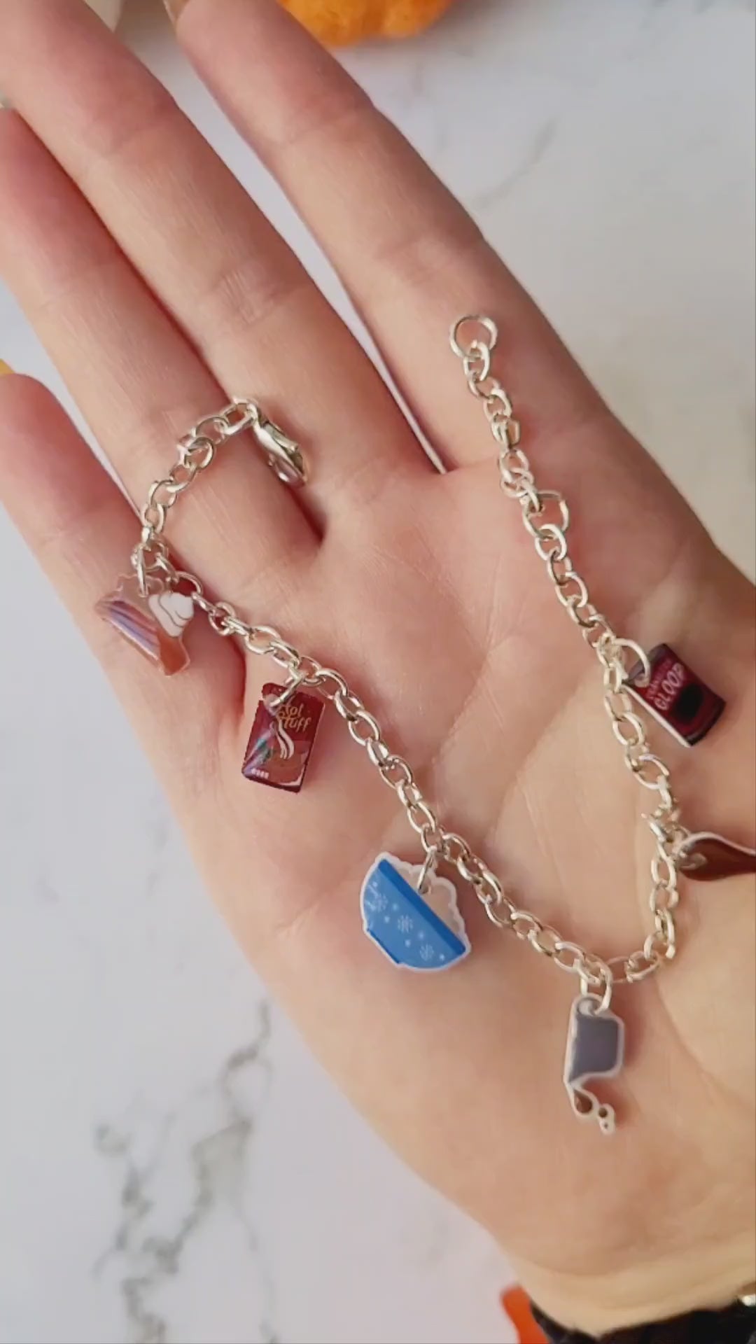 video close up of silver charm bracelet with thanksgiving themed charms on a marble background. 