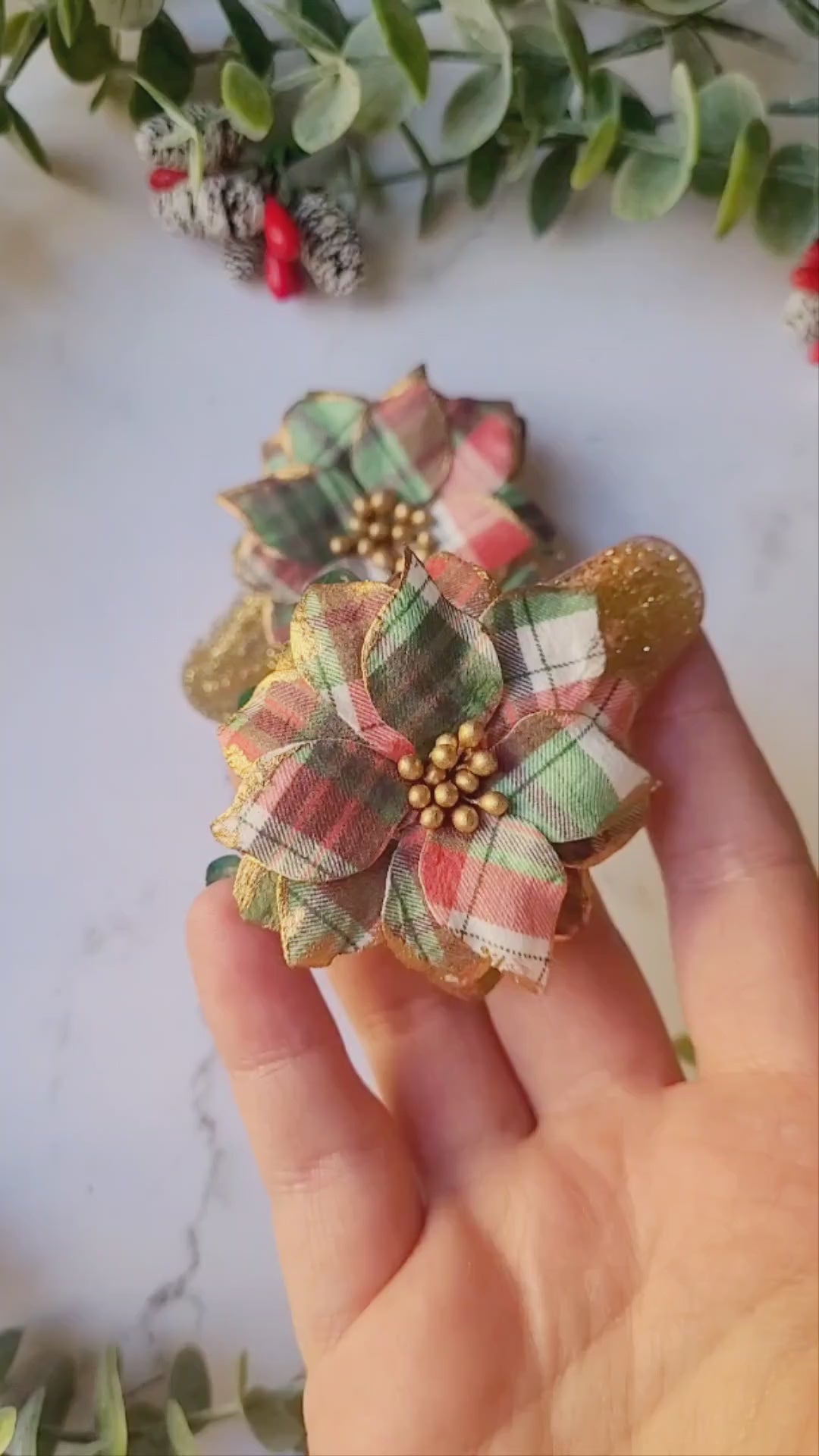 video close up of Christmas themed plaid poinsettia hair clip on a marble background. 