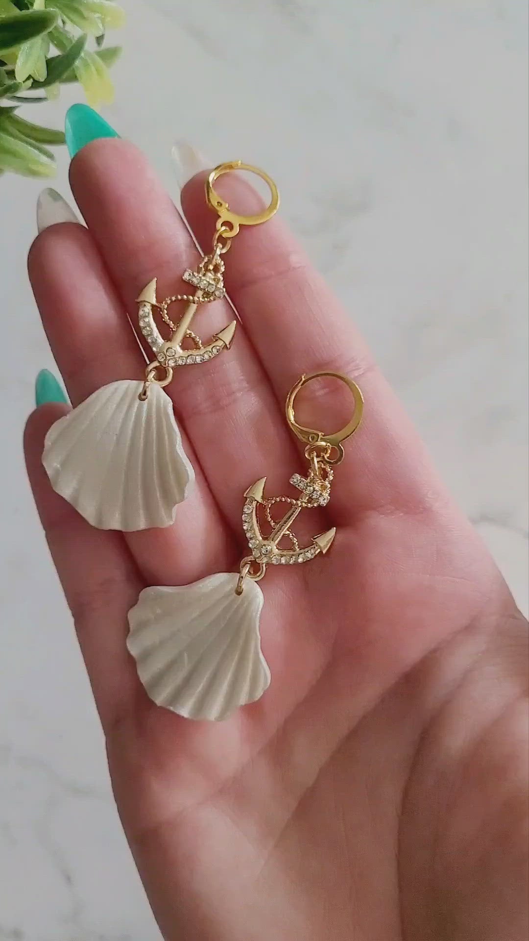 Close up of earrings with gold anchor charm and polymer clay sea shell
