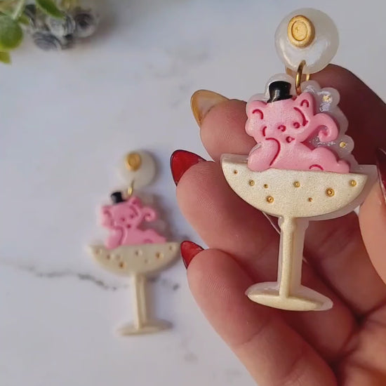 video close up of Pink Elephant in a champagne coupe earrings on a marble background . 