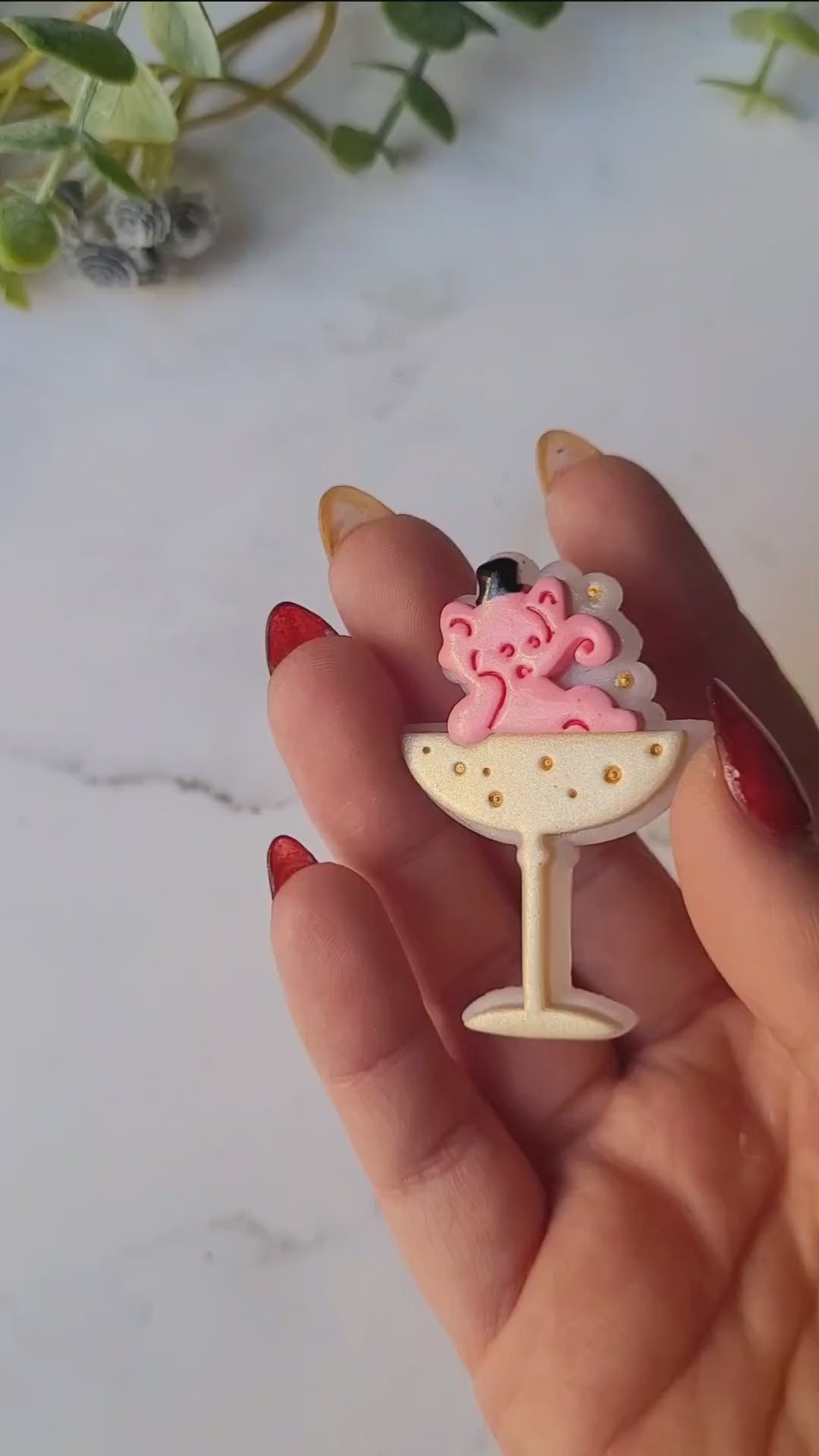 video close up of Pink Elephant in a champagne coupe brooch on a marble background .