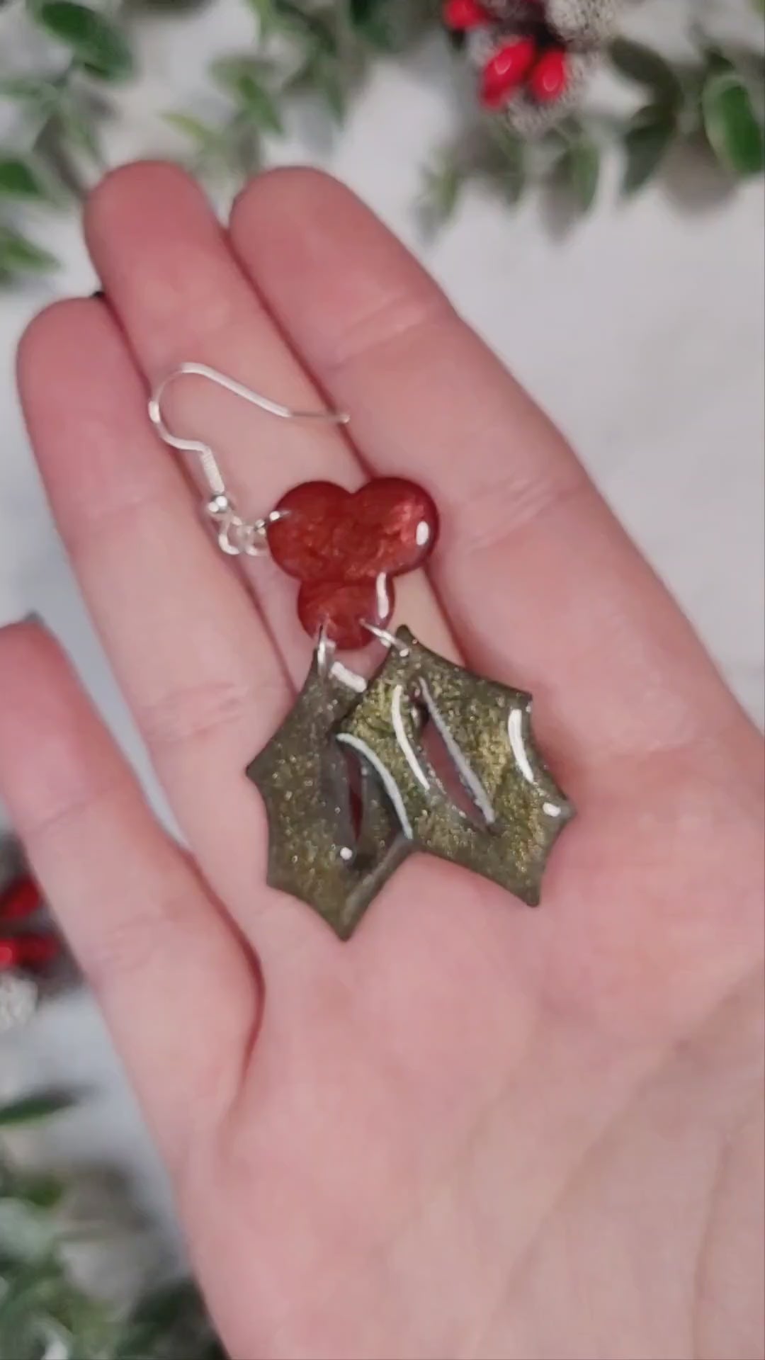 video close up of Glitter holly sprig earrings on a marble background. 