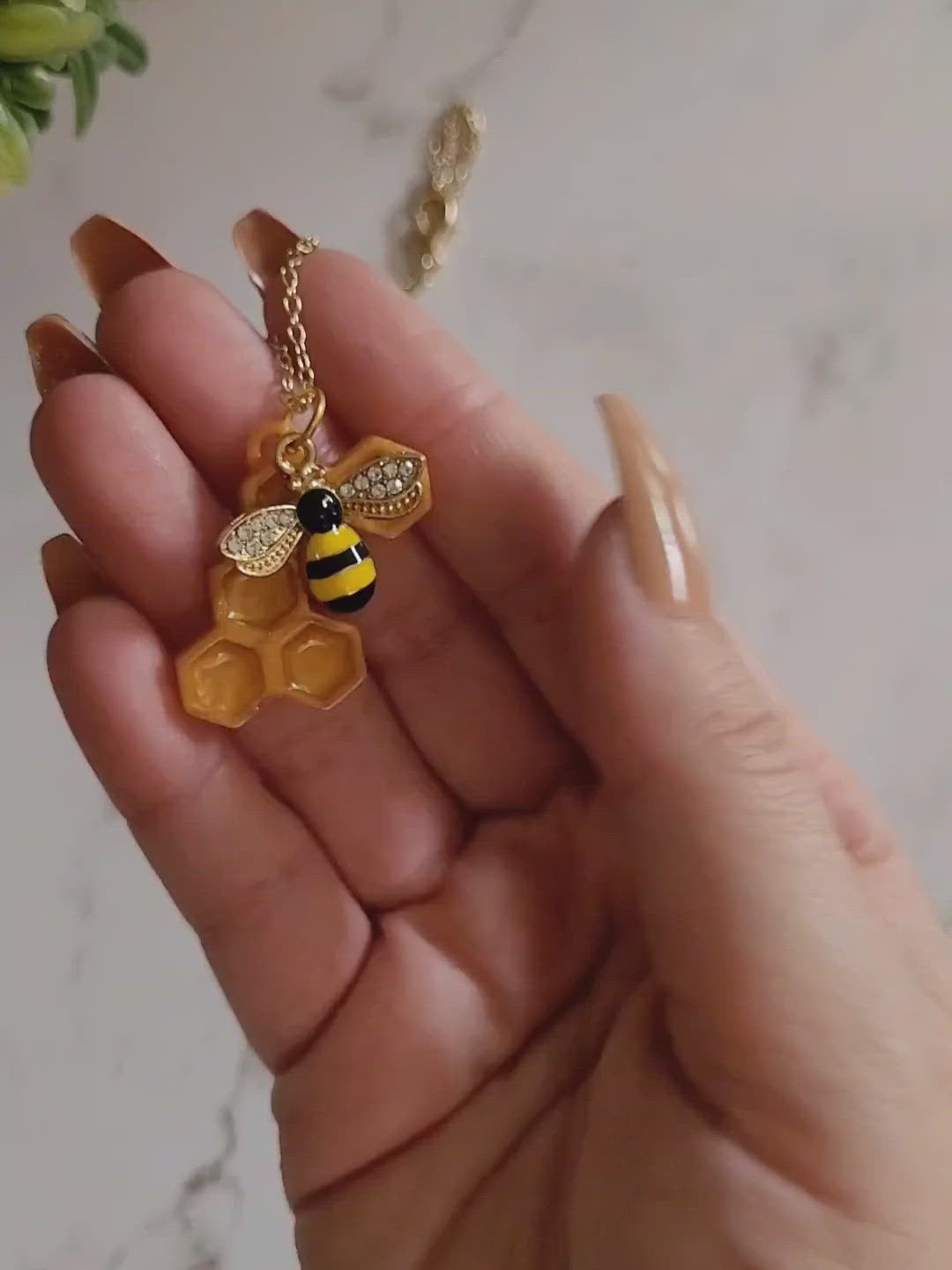 Closeup of honeycomb shaped resin necklace with bee charm in a hand to show size and color details. 