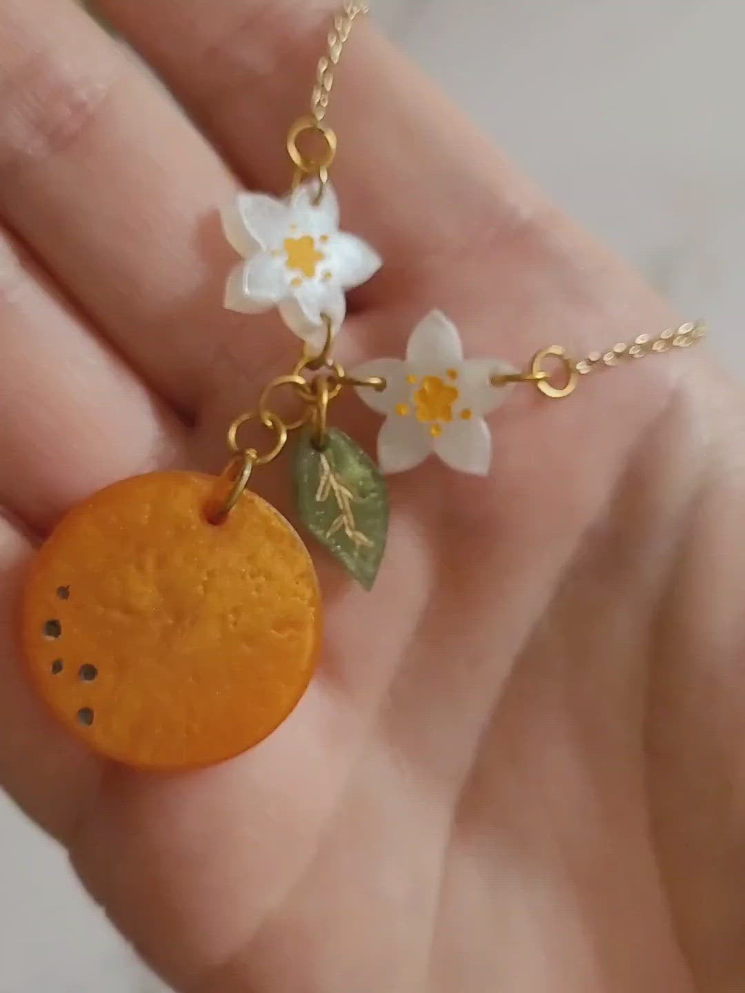 Closeup of resin orange blossom necklace in palm of hand to show size and color detail. 