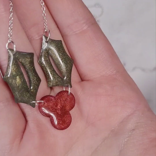 video close up of Glitter holly sprig necklace on a marble background surrounded by foliage,