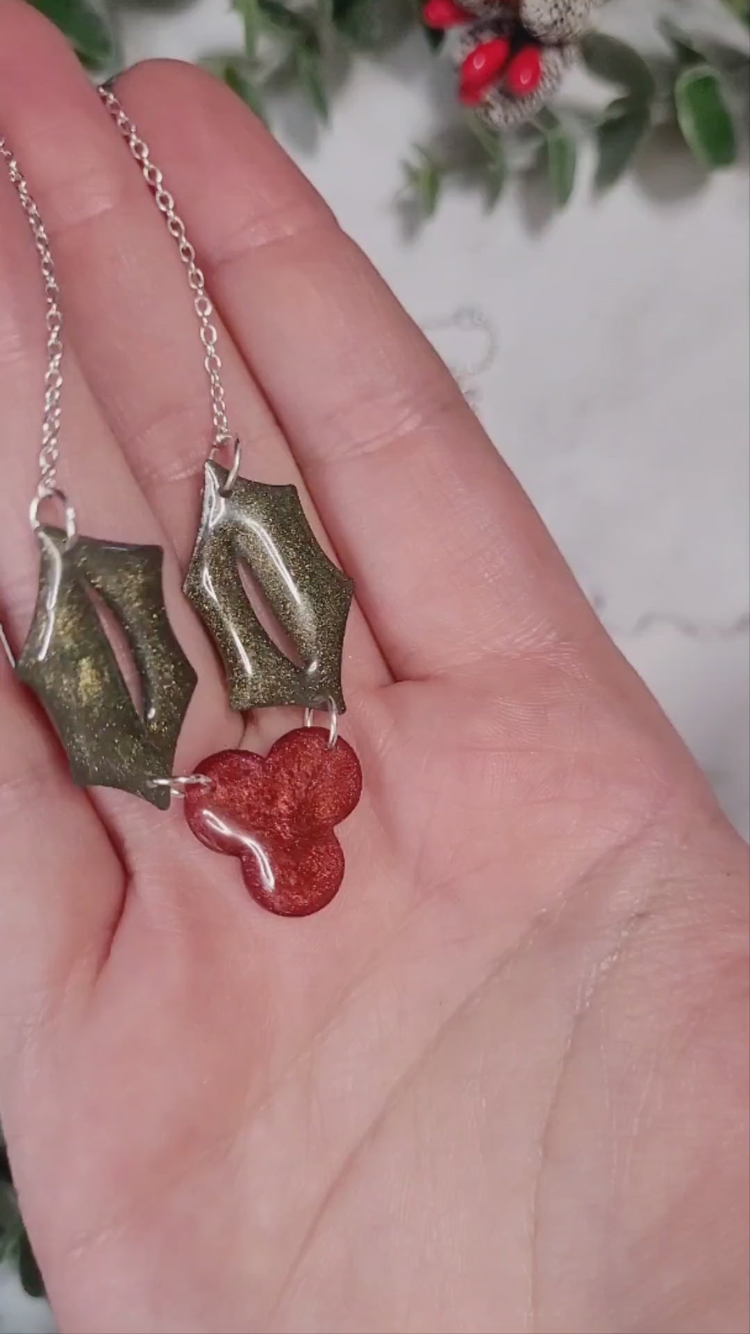 video close up of Glitter holly sprig necklace on a marble background surrounded by foliage,