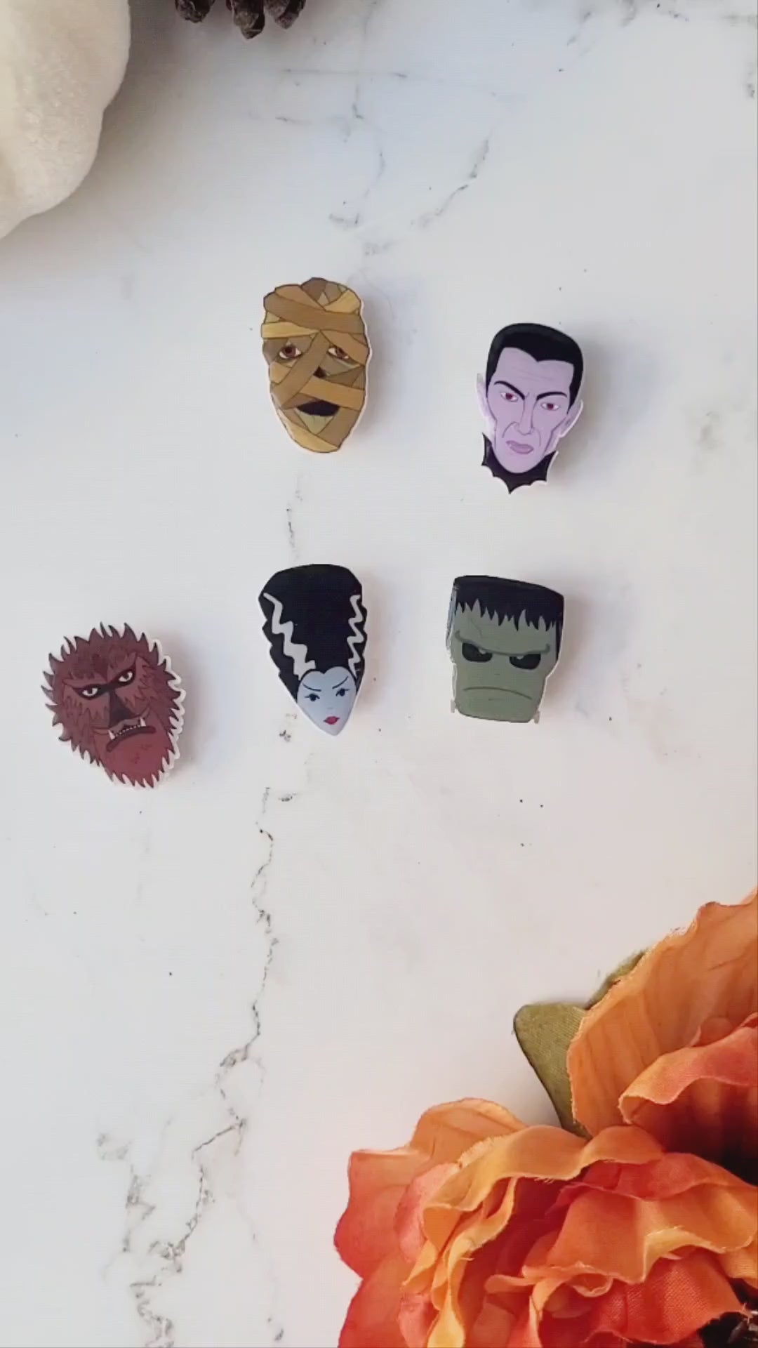video closeup of 6 universal monster head lapel pins on a marble background