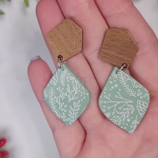 video close up of mint green winter botanical earrings on a marble background surrounded by foliage.