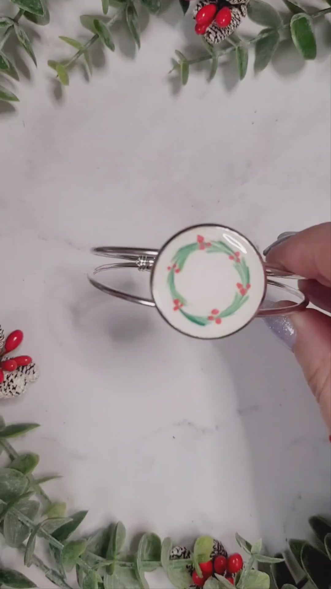video close up of silver mistletoe bracelet on a marble background surrounded by foliage.