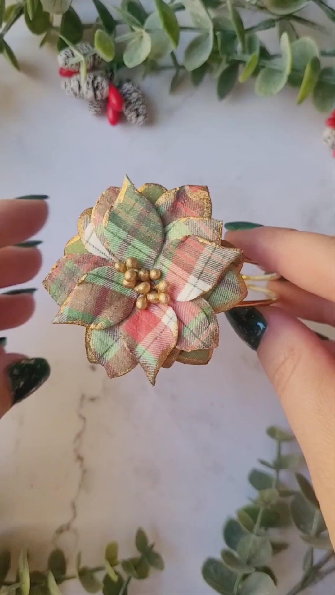 video close up of the Christmas themed plaid poinsettia bracelet on a marble background surrounded by foliage.
