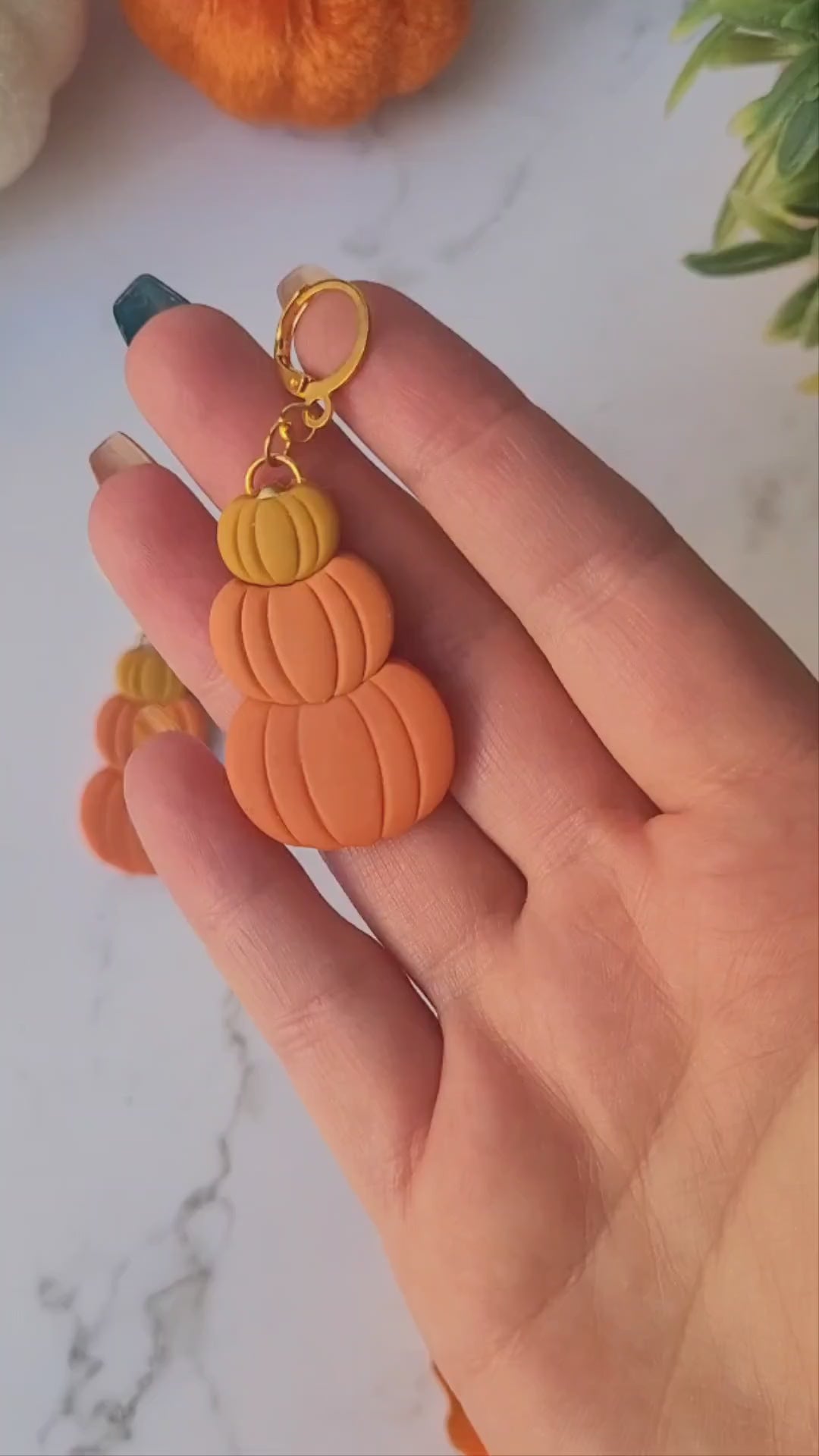 video close up of Triple stack pumpkin earrings on a marble background with fall foliage.