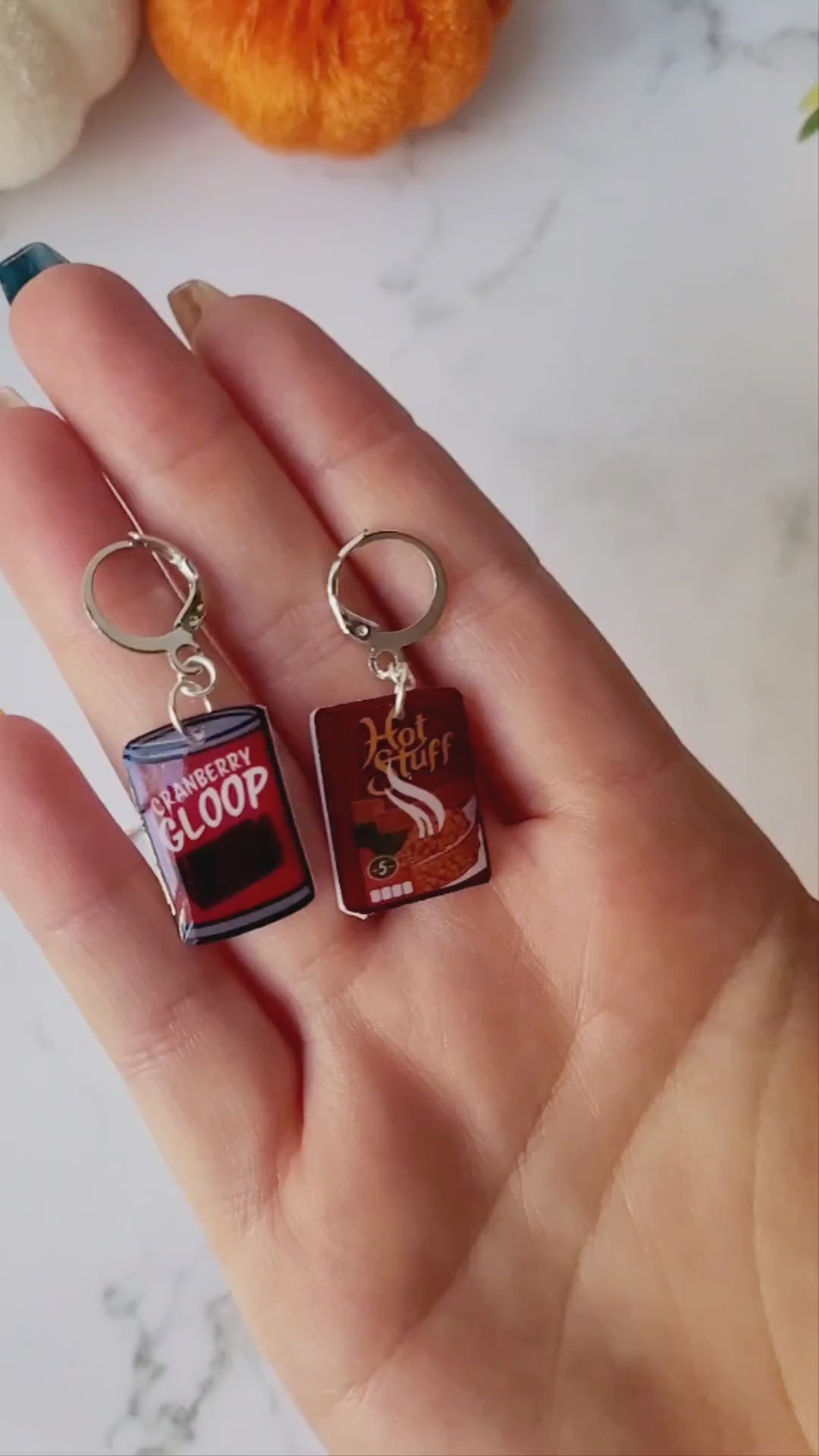 video close up of Cranberry sauce and stuffing box earrings on a marble background with fall foliage.