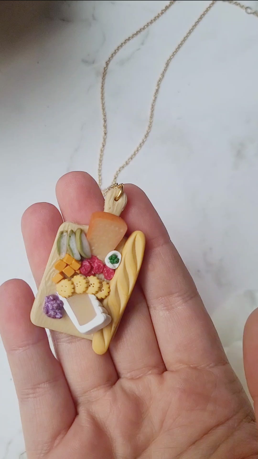 video close up of Charcuterie board necklace on a white marble background.