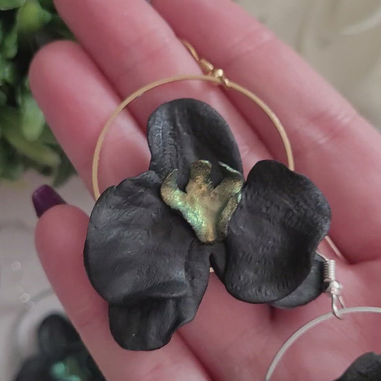 Closeup of three color variations in palm of hand. Earrings are made of black polymer clay in the shape of an orchid. 