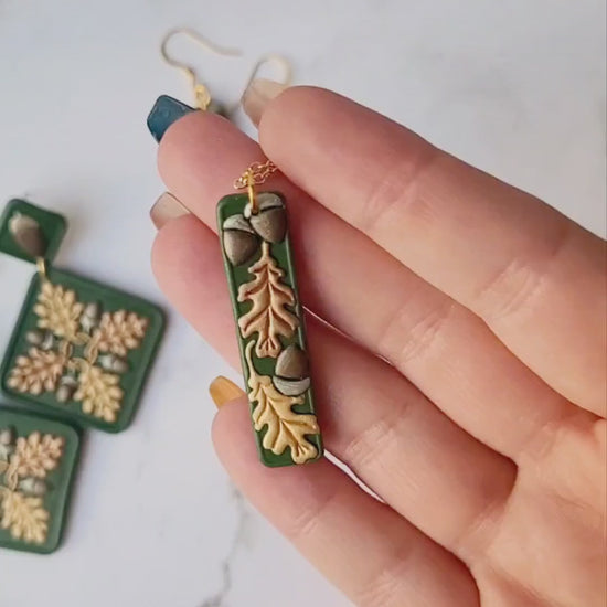 video close up of the Green bar shaped pendant with metallic acorns and oak leaves.