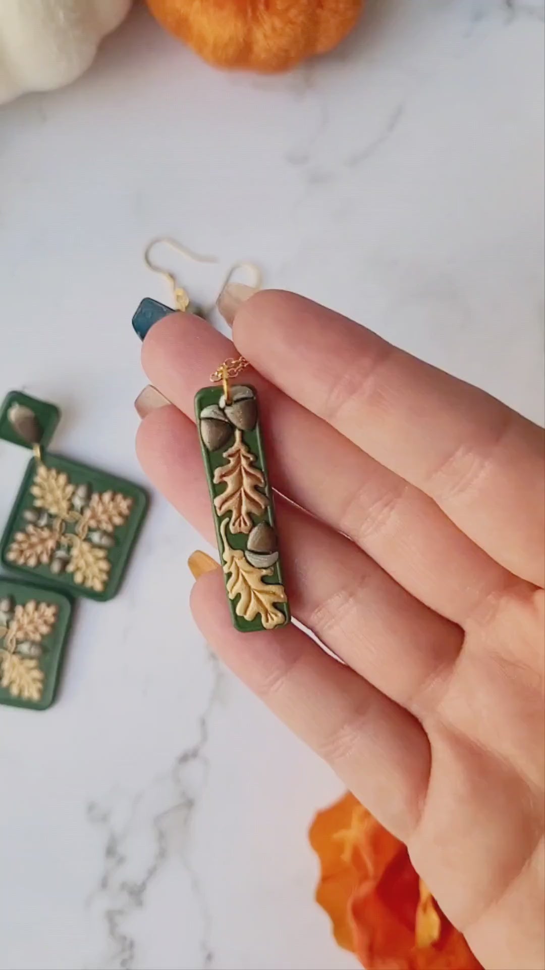 video close up of the Green bar shaped pendant with metallic acorns and oak leaves.