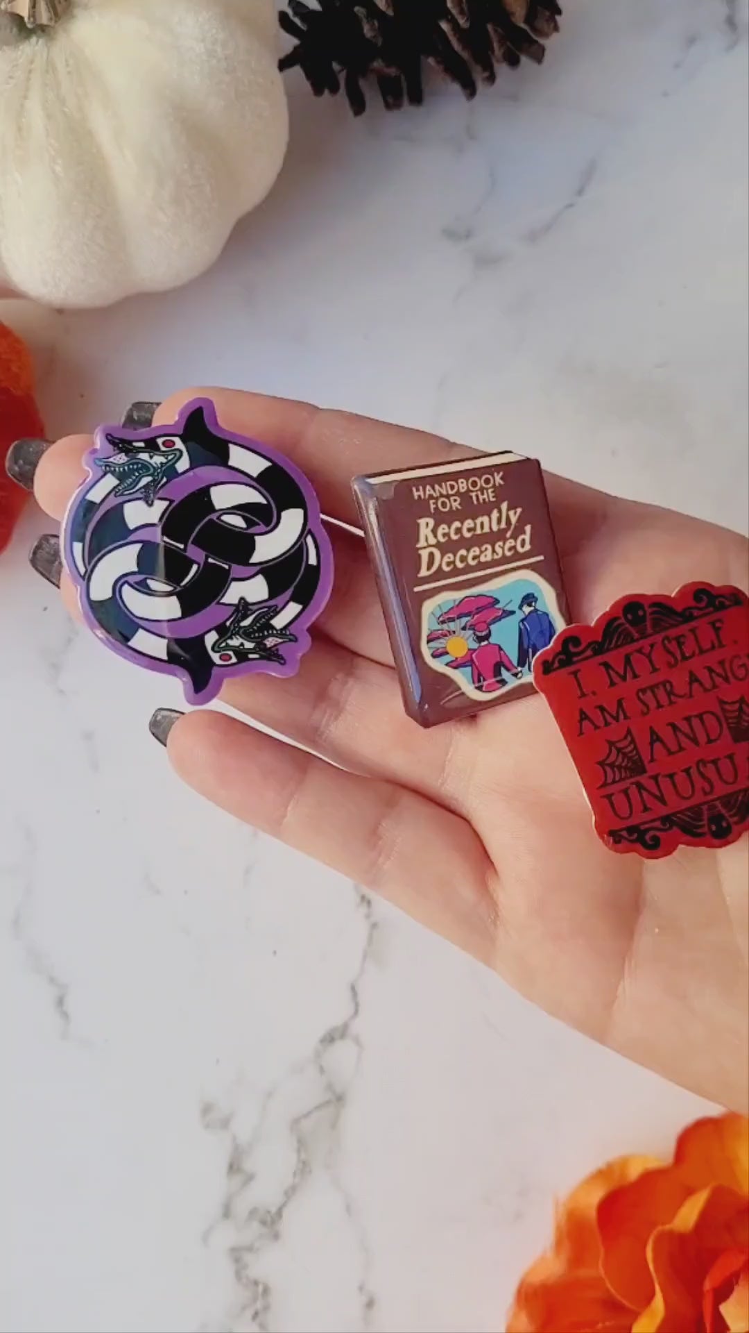 close up of three beetlejuice themed brooches on a white marble background